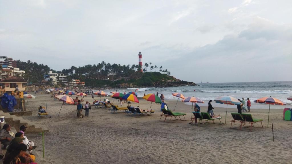 a group of people sitting on a beach with umbrellas at Vedantha Inn in Kovalam
