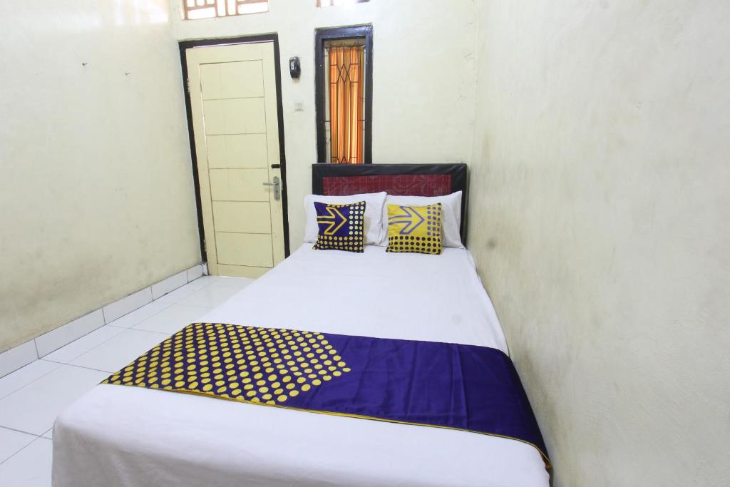 a small bedroom with a bed with blue and yellow pillows at OYO Life 93260 Bale Kosan in Tanjung