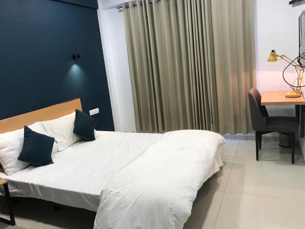 um quarto com uma cama branca com paredes azuis e uma secretária em Hooliv 7 Avenues G Block em Pune