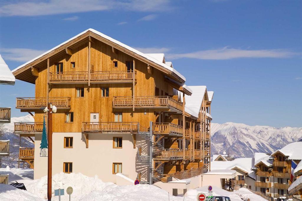 un grand bâtiment en bois dans la neige dans l'établissement Madame Vacances Les Balcons Des Airelles, aux Orres