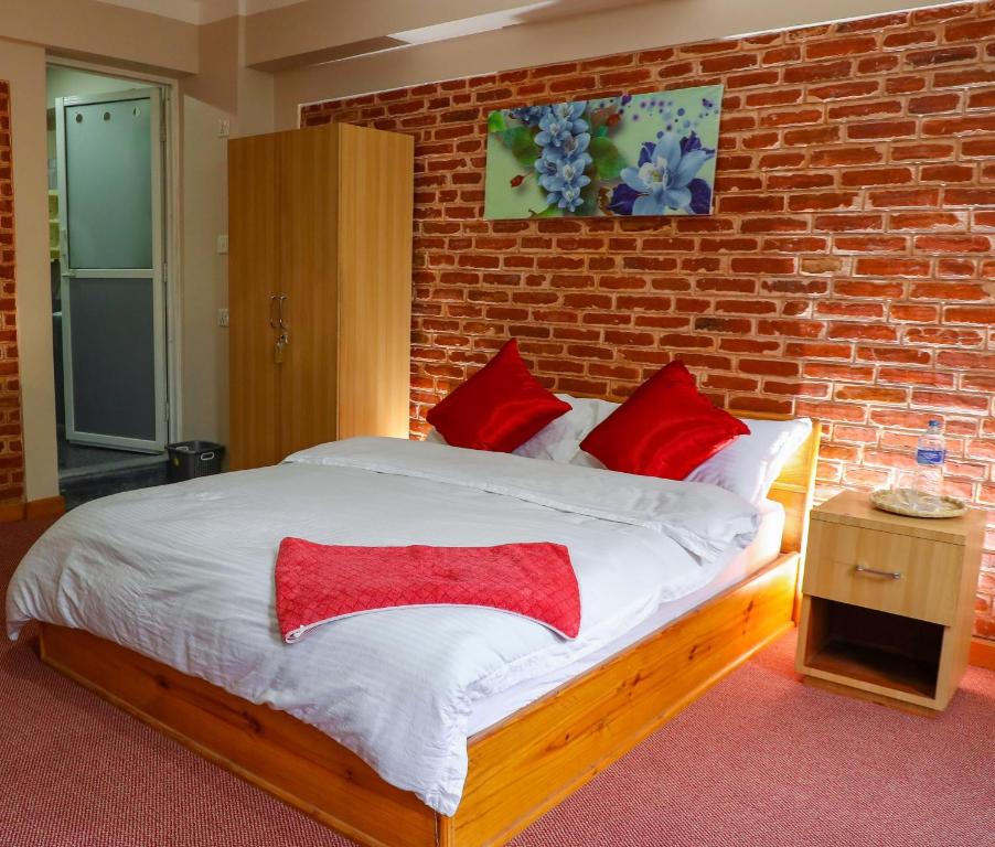 - une chambre avec un mur en briques et un lit avec des oreillers rouges dans l'établissement Kaji Chen, The Tourist Accommodation, à Pātan