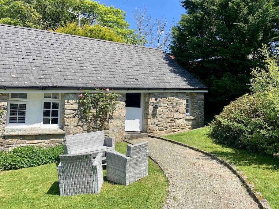 dwa wiklinowe krzesła siedzące przed kamiennym domem w obiekcie Grooms cottage, a tranquil Cornish retreat w mieście Lanteglos