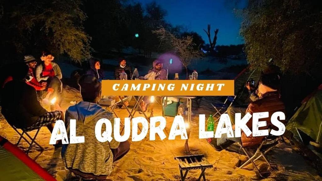 a group of people standing around a tent at night at Al Qudra Lakes Camping by Hyba in Dubai