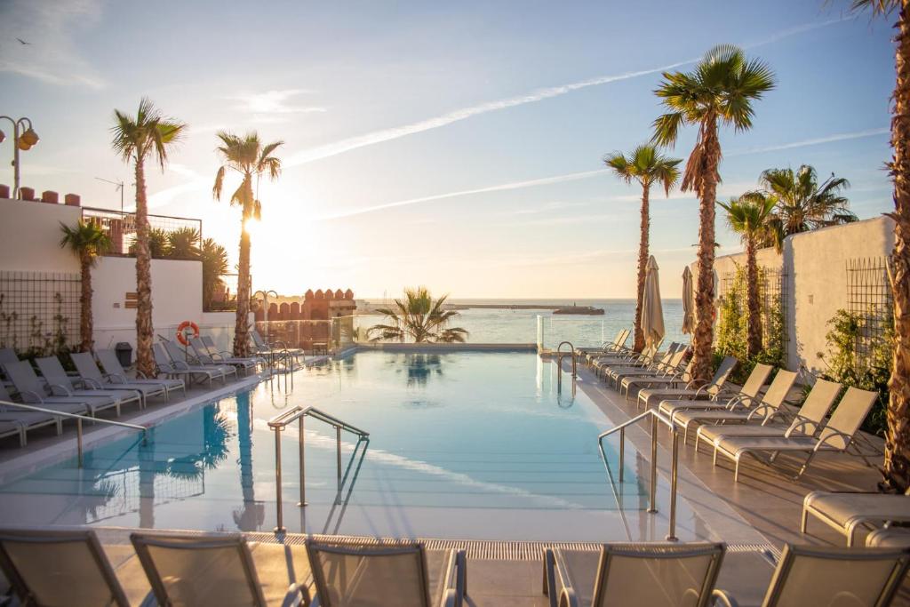 una piscina con sillas y palmeras en Hotel Benalmadena Beach, en Benalmádena