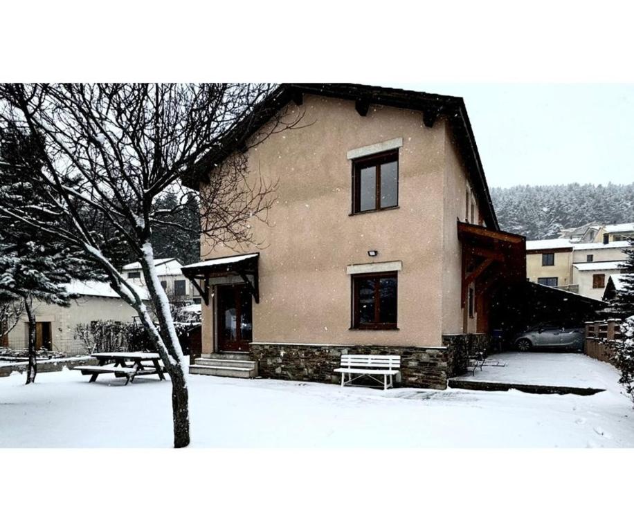un bâtiment dans la neige avec un banc devant dans l'établissement La Granja - Maison avec cheminée, jardin, baby-foot, à Formiguères