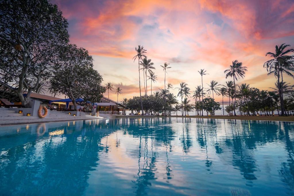 a swimming pool with palm trees and a sunset at Pegasus Reef - A Beach Resort in Colombo in Colombo
