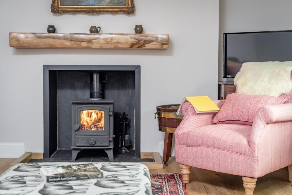 a living room with a fireplace and a pink chair at Burnside - gorgeous romantic cottage for 2 in Monzie