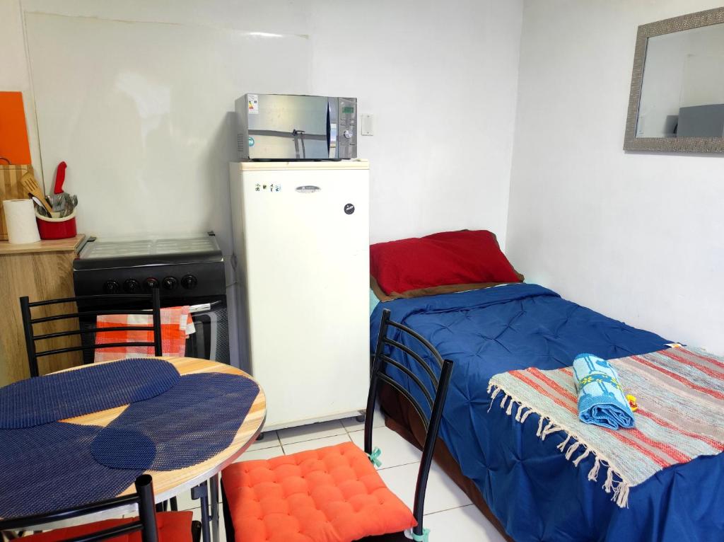 a small room with a bed and a table and a refrigerator at Cabaña Playera cómoda y central in Viña del Mar