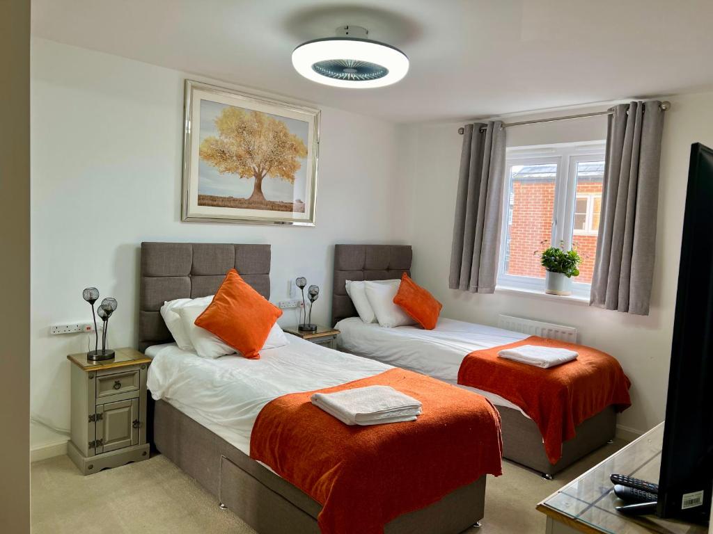 una camera con 2 letti, lenzuola arancioni e TV di Driver Way a Wellingborough