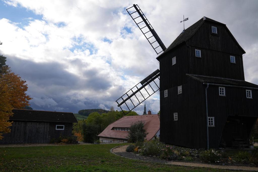 eine schwarze Scheune mit einer Windmühle auf einem Feld in der Unterkunft Ferienwohnung An der Berndtmühle in  Oderwitz