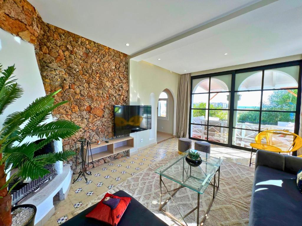 sala de estar con TV y pared de piedra. en La Finca - 3BR Seaside Villa with Private Pool & BBQ, en Tánger