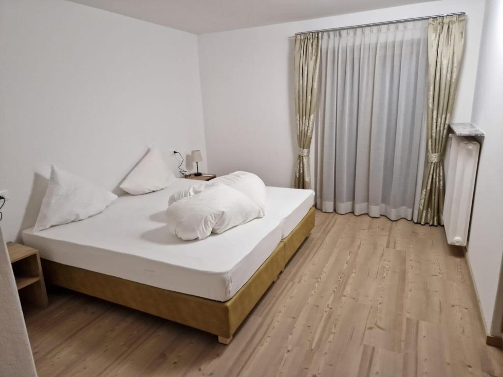 Cette chambre comprend un lit avec des draps blancs et du parquet. dans l'établissement Apartment Aghel, à Ortisei