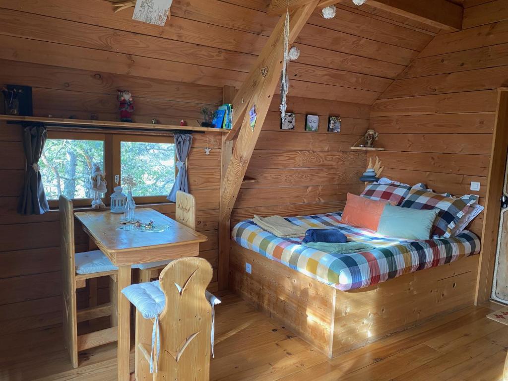 1 dormitorio en una cabaña de madera con 1 cama y 1 mesa en Les Cabanes de Maya, en Caille