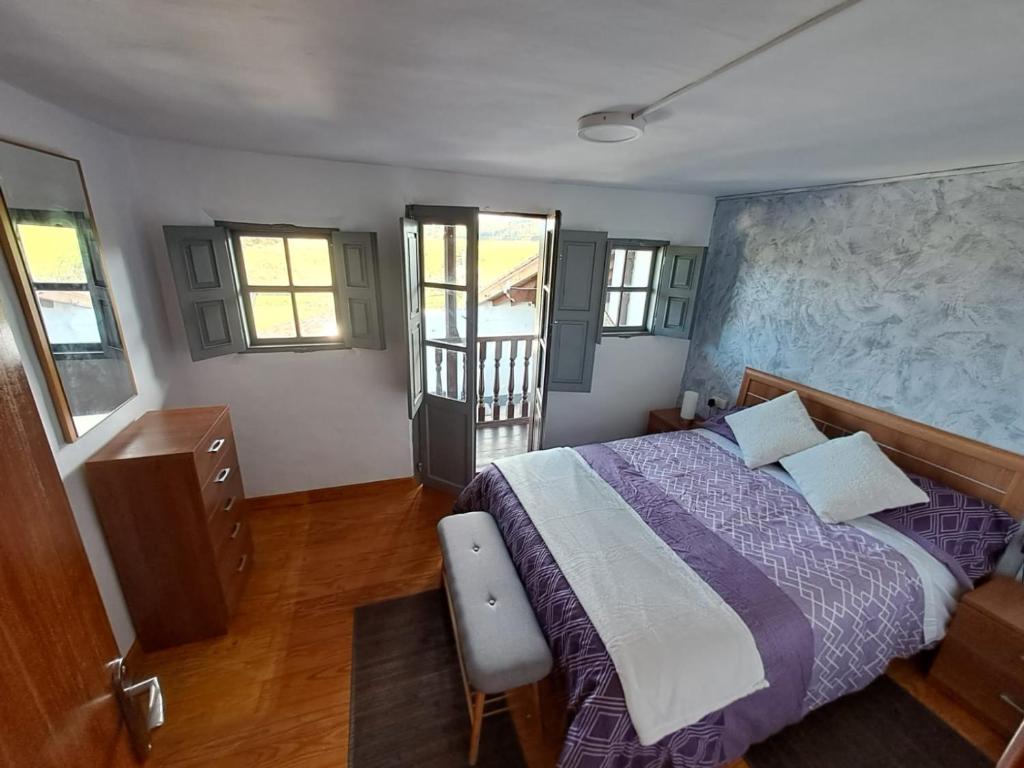 1 dormitorio con cama morada y pared con ventanas en La Corralada de Merón, en San Vicente de la Barquera