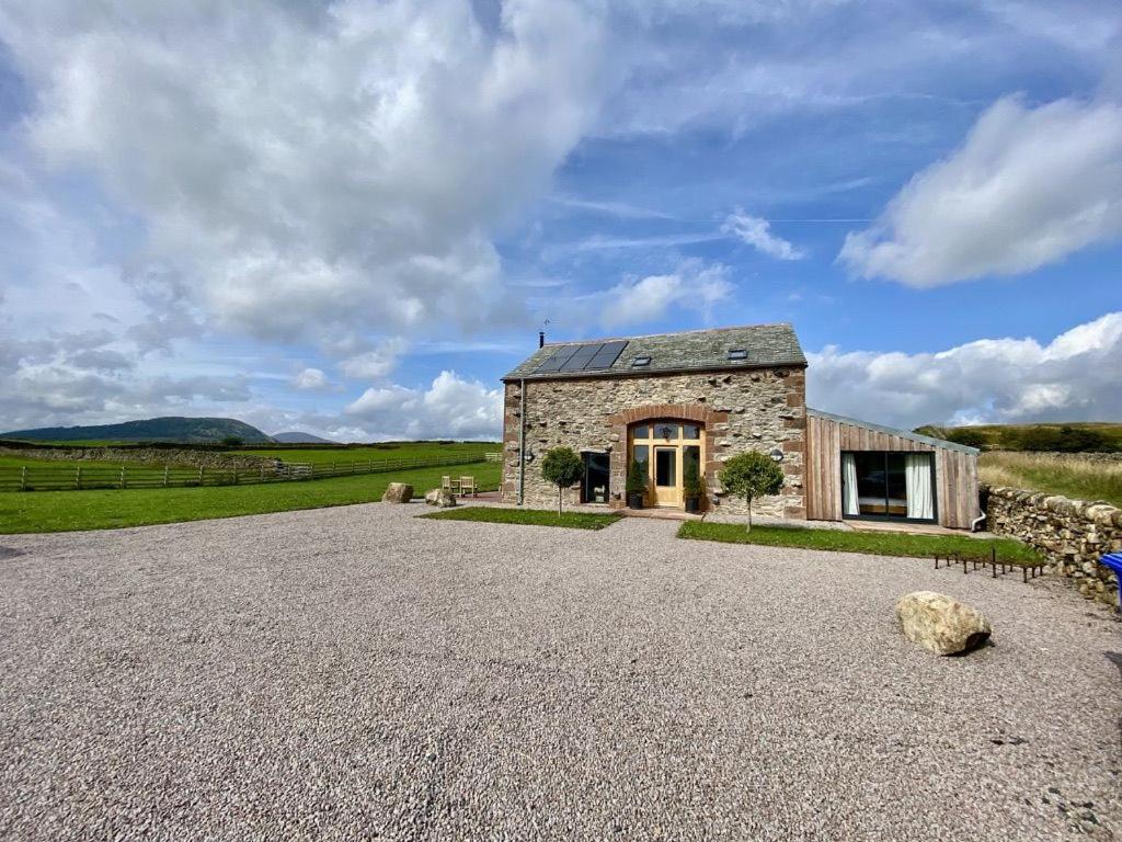 a stone house in a field with a gravel driveway at Sheepfold Barn in Penruddock