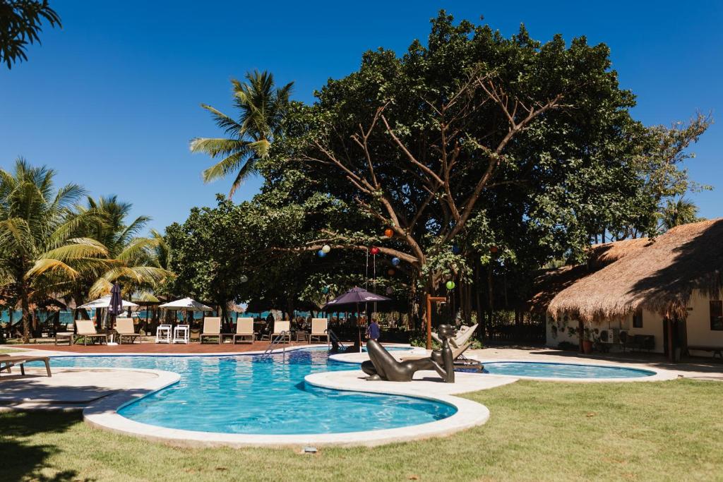 a resort swimming pool with chairs and a thatched building at Bangalôs do Gameleiro in Praia dos Carneiros