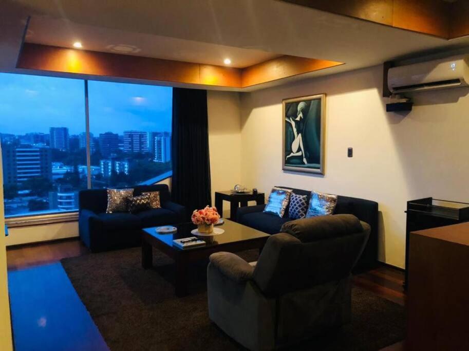 un soggiorno con divani, tavolo e ampia finestra di apartamento avenida las américas a Guatemala