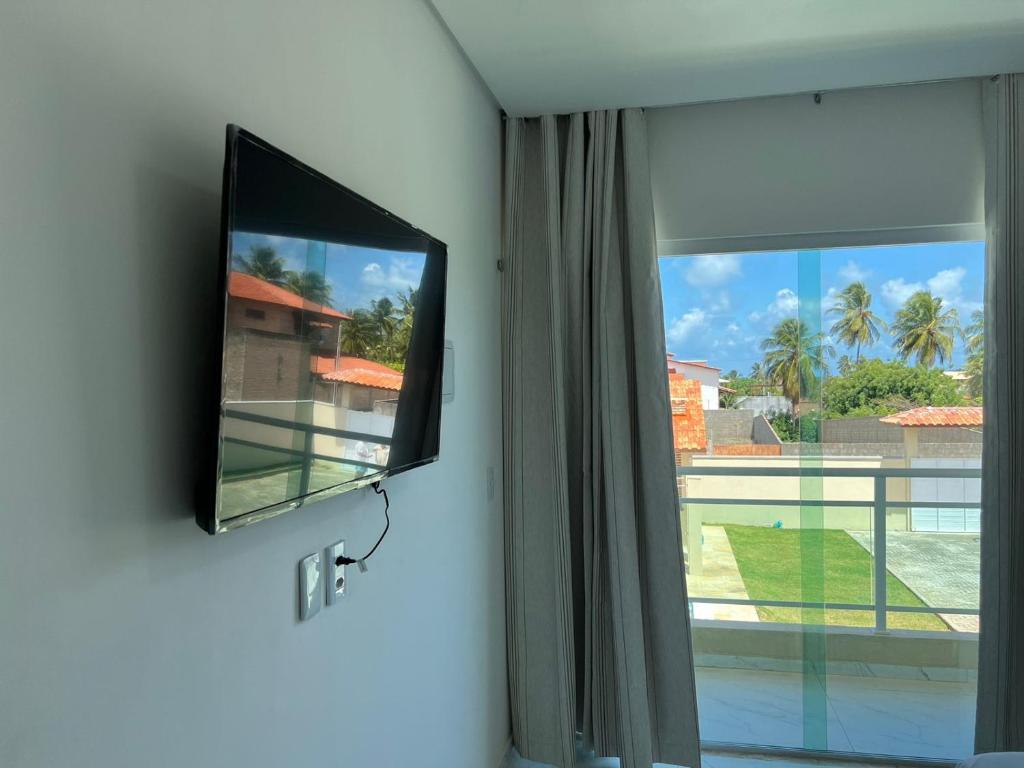 TV de pantalla plana colgada en una pared junto a una ventana en Meu Chale Flecheiras en Flecheiras