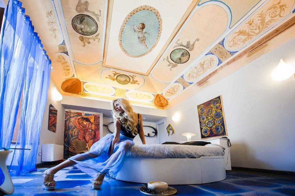 una mujer sentada en una cama en una habitación con techos pintados en Suite D'Autore Art Design Gallery, en Piazza Armerina
