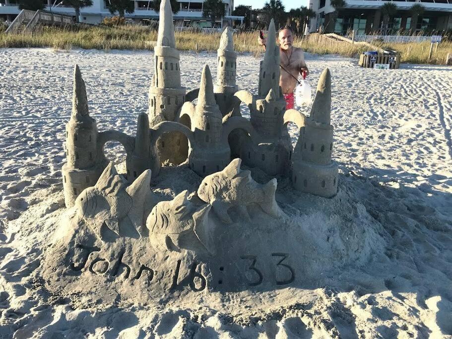 a child standing in front of a sand castle on the beach at Oceanfront Get Away in Myrtle Beach