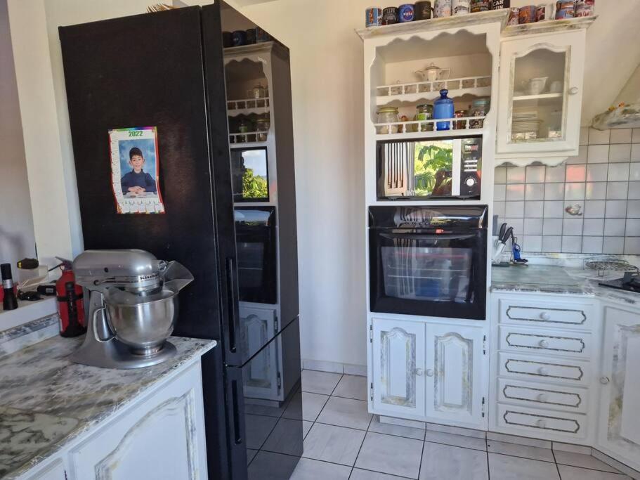 a kitchen with white cabinets and a black refrigerator at La maison du Pêcheur in Terre-de-Haut