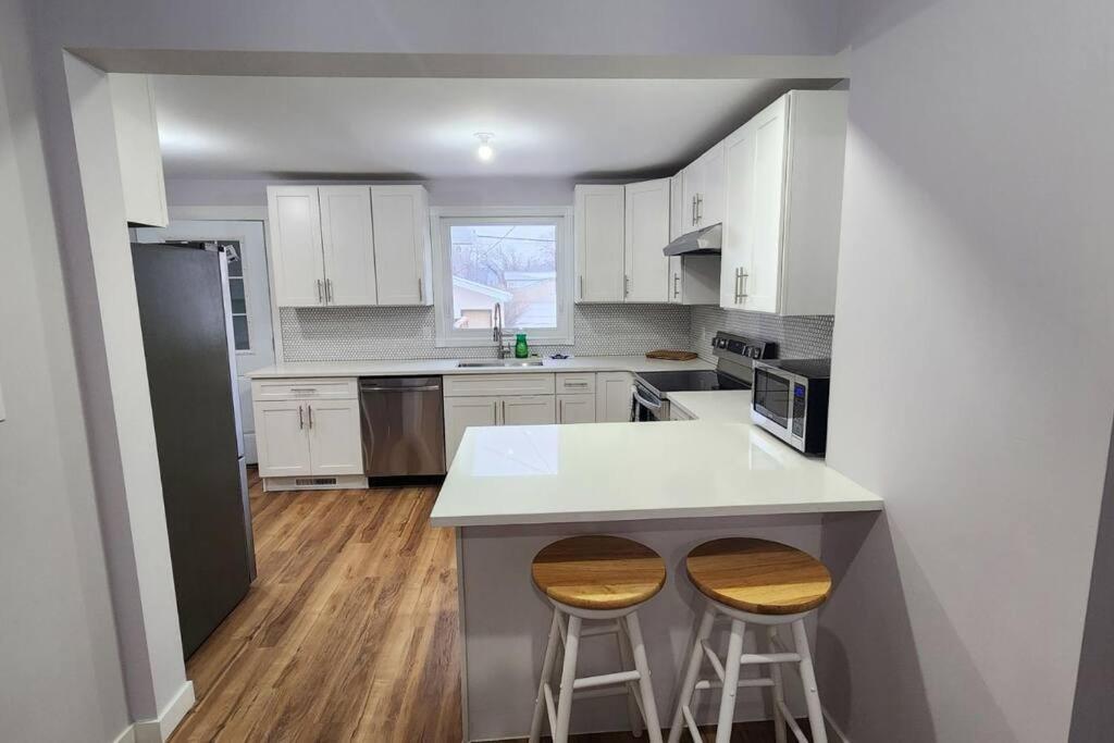 una cocina con armarios blancos y una barra con 2 taburetes en St B. Living, en Winnipeg
