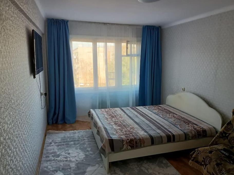 a bedroom with a bed and a window with blue curtains at Сozy apartment,16-1 Satpayev in Ustʼ-Kamenogorsk