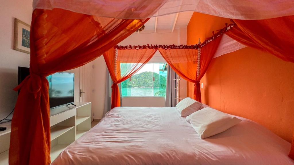 ein Schlafzimmer mit einem Bett mit orangefarbenen Wänden und einem Fenster in der Unterkunft Casa com vista a praia da Barra do Sahy in Barra do Sahy