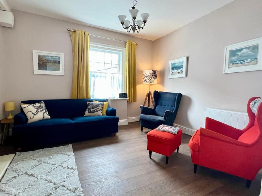 een woonkamer met een blauwe bank en rode stoelen bij Beautifully decorated bright and cosy cottage in Aveton Gifford