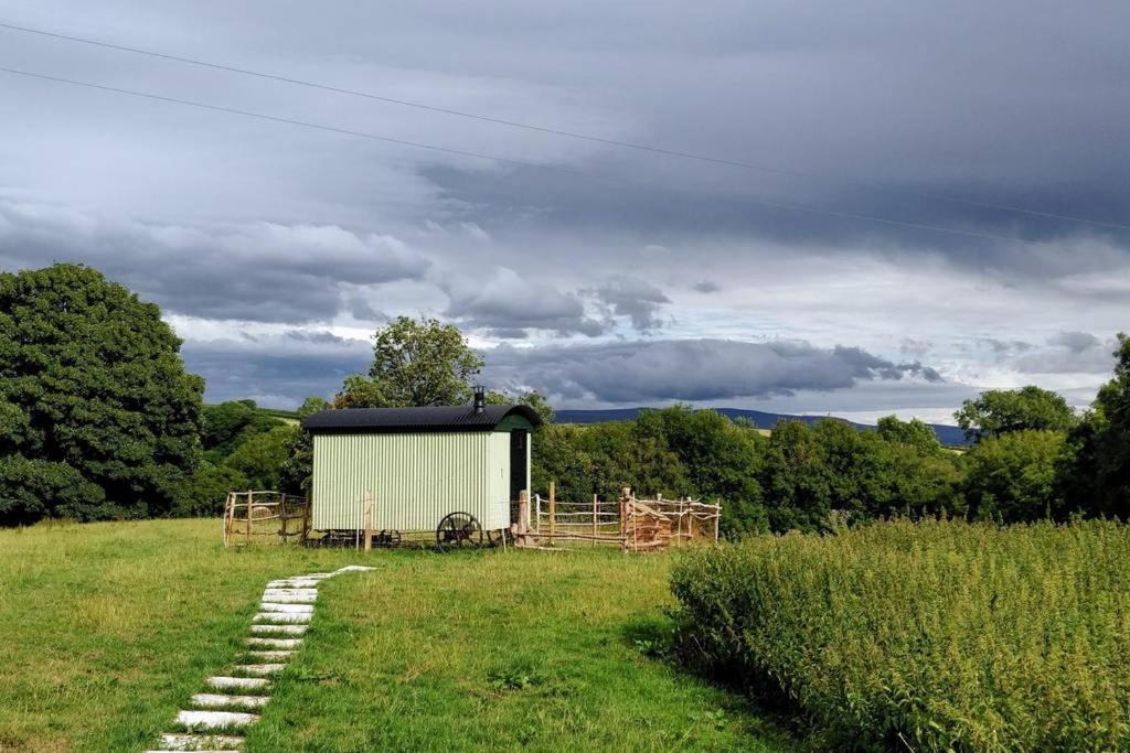 a barn in a field with a stone path at Cefnmachllys Shepherds Huts in Brecon