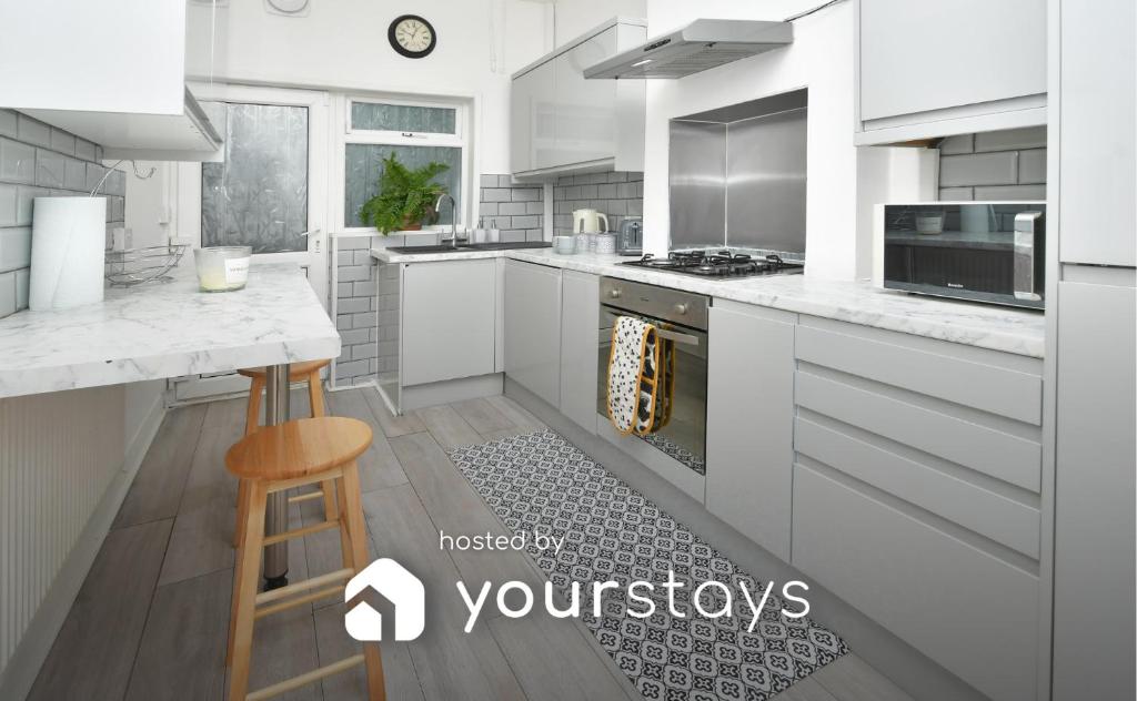 a kitchen with white cabinets and a counter with a stool at Frilsham House by YourStays in Stoke on Trent