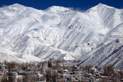 a snow covered mountain range with trees in the foreground at Los Coirones in Potrerillos