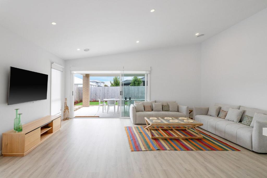a white living room with a couch and a tv at Escape by the Bay in Coronet Bay