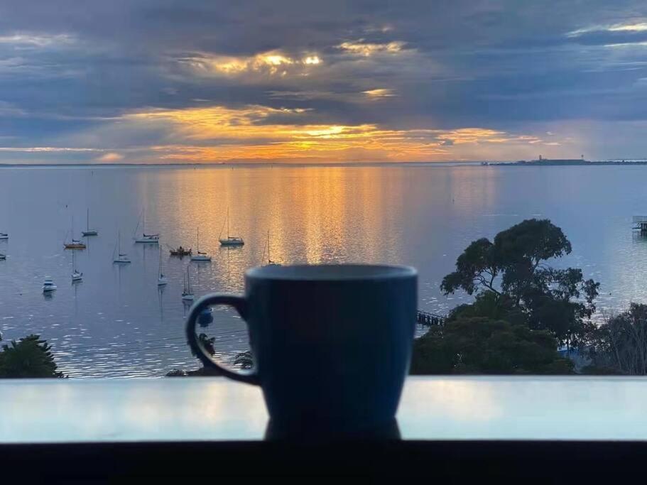 a coffee cup sitting on a window sill with a view of the water at 2 Bedrooms Aptmt with Ocean View in Geelong