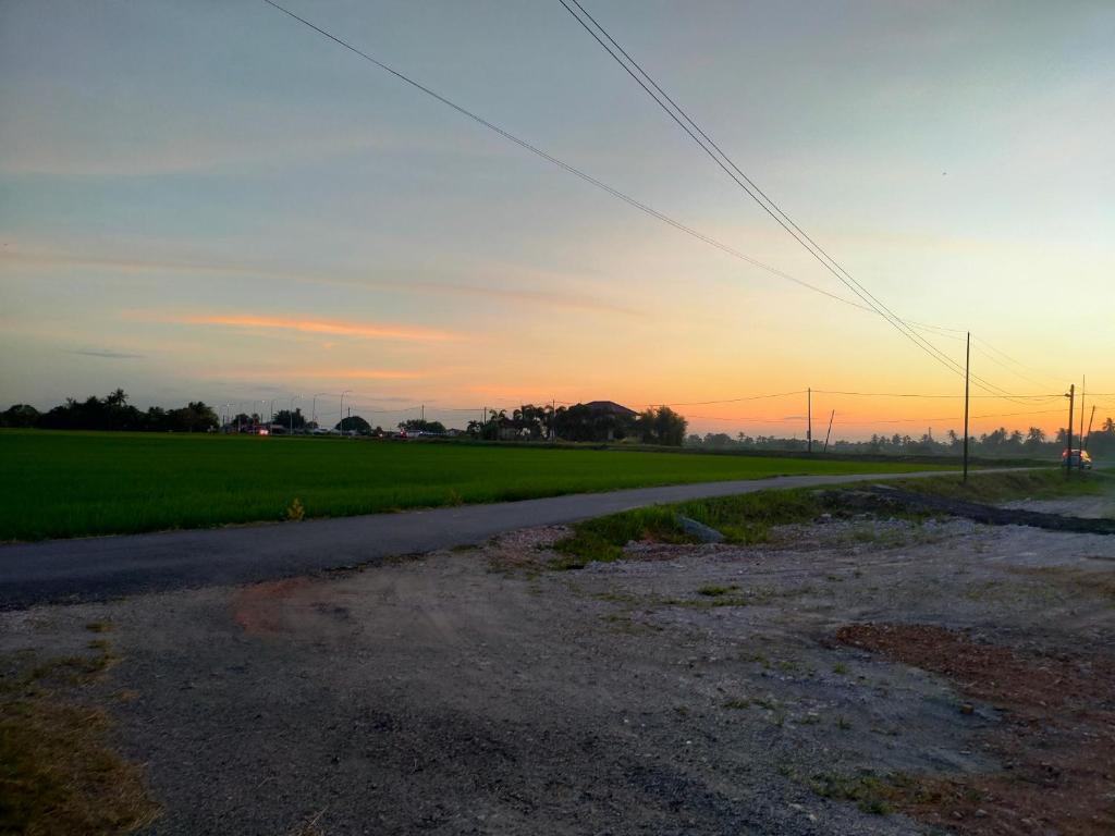 an empty road next to a green field at sunset at Homestay Midan Alor Setar in Alor Setar