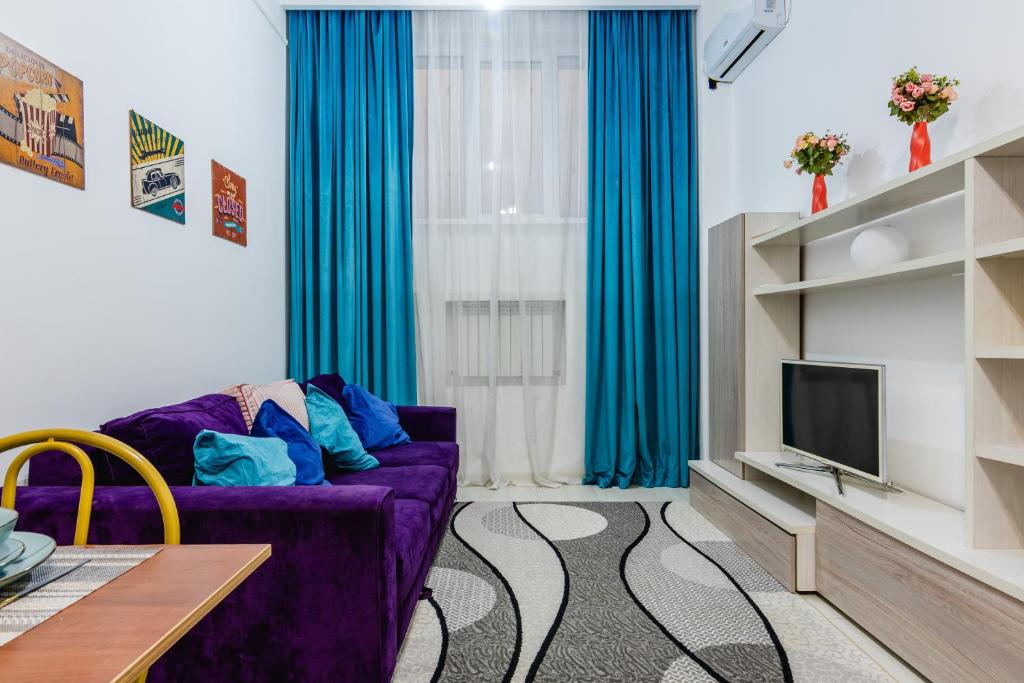 sala de estar con sofá púrpura y TV en 2 комнатная квартира в сердце города - цокольный этаж en Almaty
