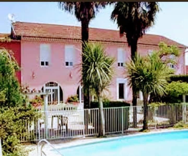 una casa rosa con palmeras y una valla en Le Castel d'olmes, en Laroque-dʼOlmes
