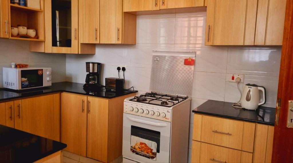 a kitchen with a white stove and wooden cabinets at Rossyln Home close to UN, Village Market and Two Rivers Mall in Nairobi