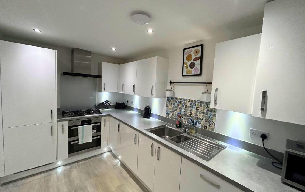 una cocina con armarios blancos y fregadero en High Wycombe Stunning Stylish Four Bedroom House en High Wycombe