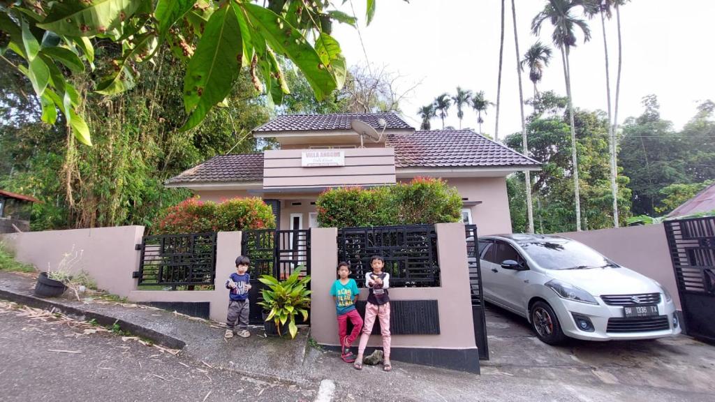 tres niños parados frente a una casa en Vila Anggur Pintukabun, en Bukittinggi