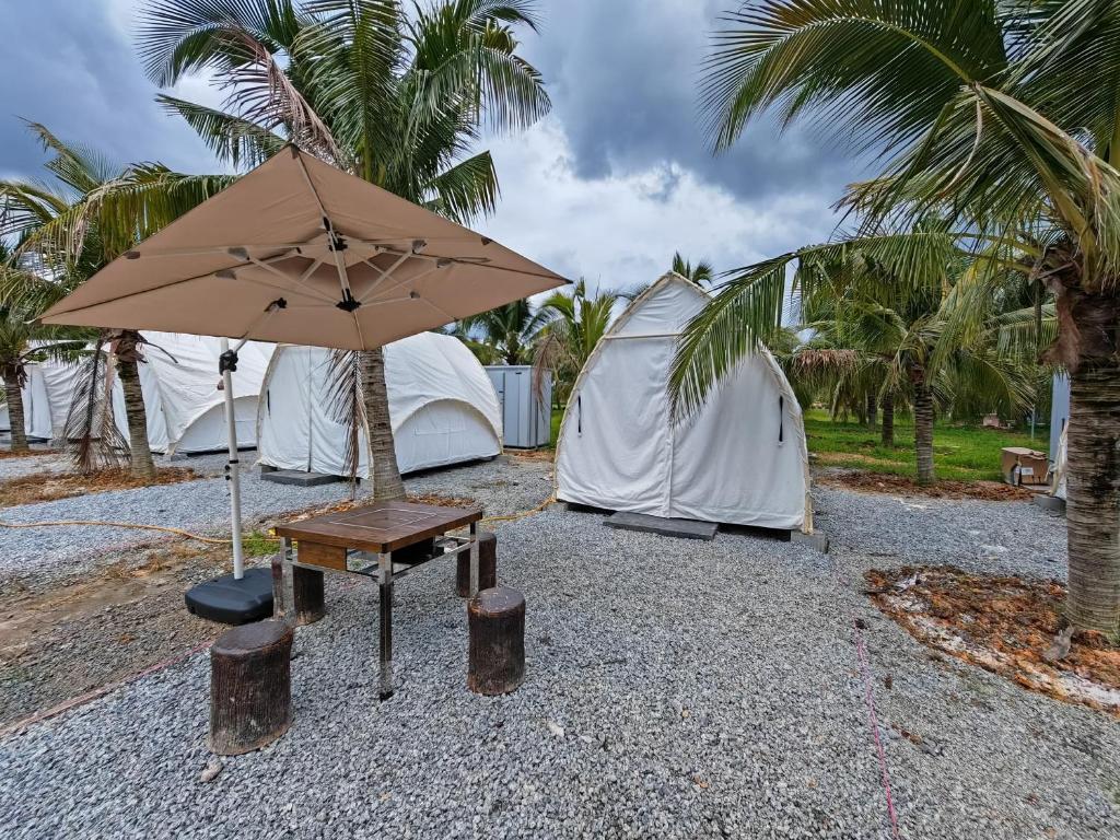 stolik z parasolką przed namiotami w obiekcie The Coco Journey - Eco Tent w mieście Kelebang Besar