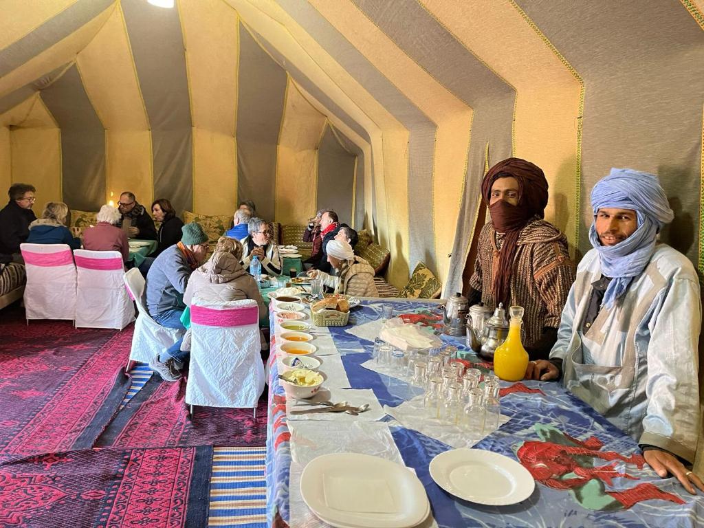 un gruppo di persone sedute a un lungo tavolo di Titanic hôtel restaurant & désert excursions lac irik a Foum Zguid