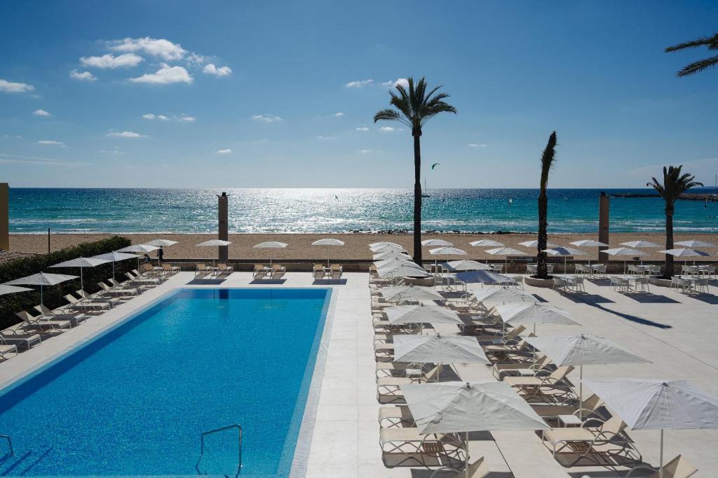 una piscina con sillas y sombrillas junto a la playa en THB El Cid - Adults Only en Can Pastilla