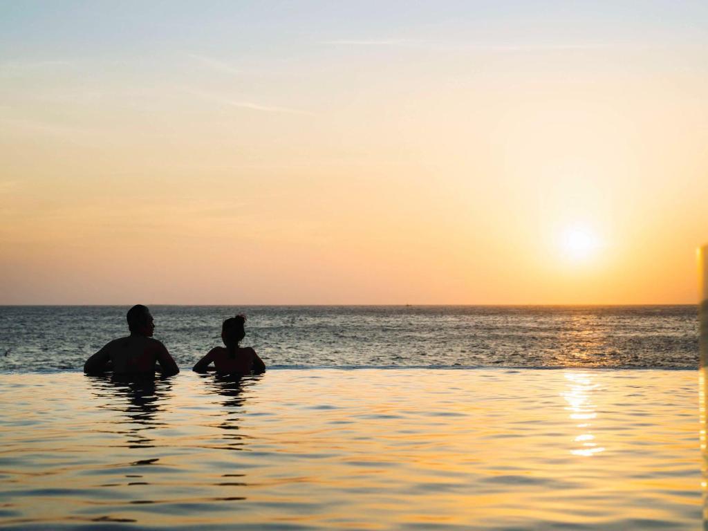 two people sitting in the ocean watching the sunset at Mercure Vung Tau Resort in Vung Tau