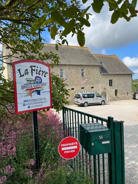 un panneau devant un bâtiment avec une voiture dans l'établissement La Fiere Bridge Guest House, à Amfreville