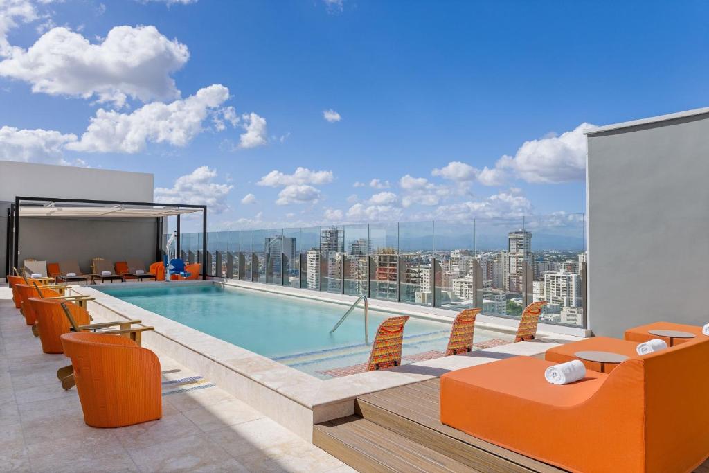 a pool on the roof of a building with orange chairs at Aloft Santo Domingo Piantini in Santo Domingo
