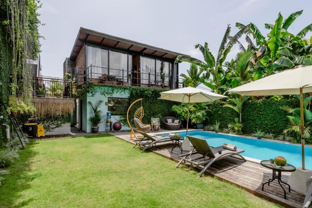 a backyard with a pool and chairs and umbrellas at Big Brother Berawa Beach in Canggu