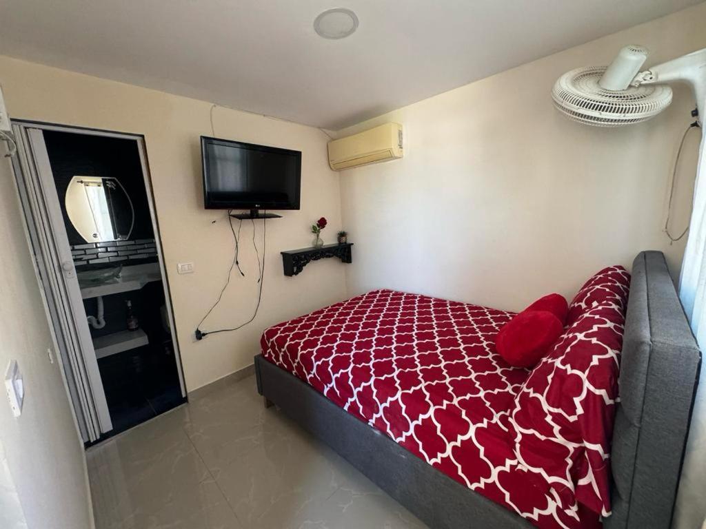 een slaapkamer met een bed met een rood dekbed en een televisie bij Hospedaje Dino in Cartagena