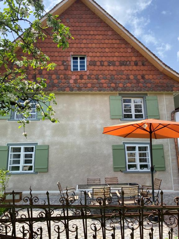 ein orangefarbener Sonnenschirm und Bänke vor einem Gebäude in der Unterkunft Gemütliches Bauernhaus am Bodensee in Deggenhausertal