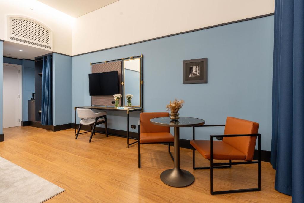 A sitting and work area with a desk, mirror, round table and two orange armchairs.